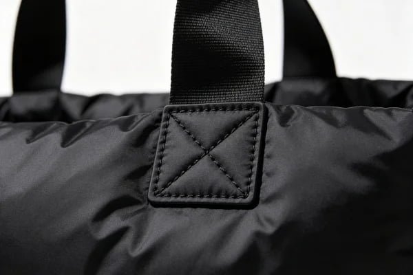 Close-up of reinforced Box-X stitching on a puffer tote bag handle attachment area